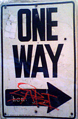 One way sign with a white sticker a black sticker with the letters hem and writing consisting of SAPZT