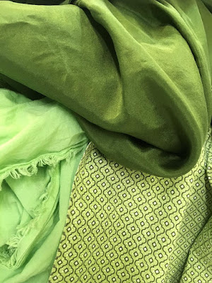 Three green fabrics piled together, one thin, soft, and shiny grass-green; one a thin apple-green cotton, and one a thicker cotton with a small black ogee print over light green.