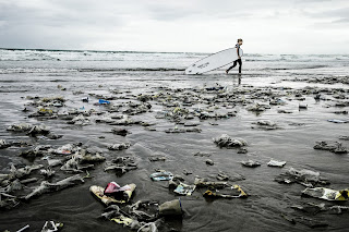 Ironic picture of nasty plastic trash on a beach with a plastic surfboard