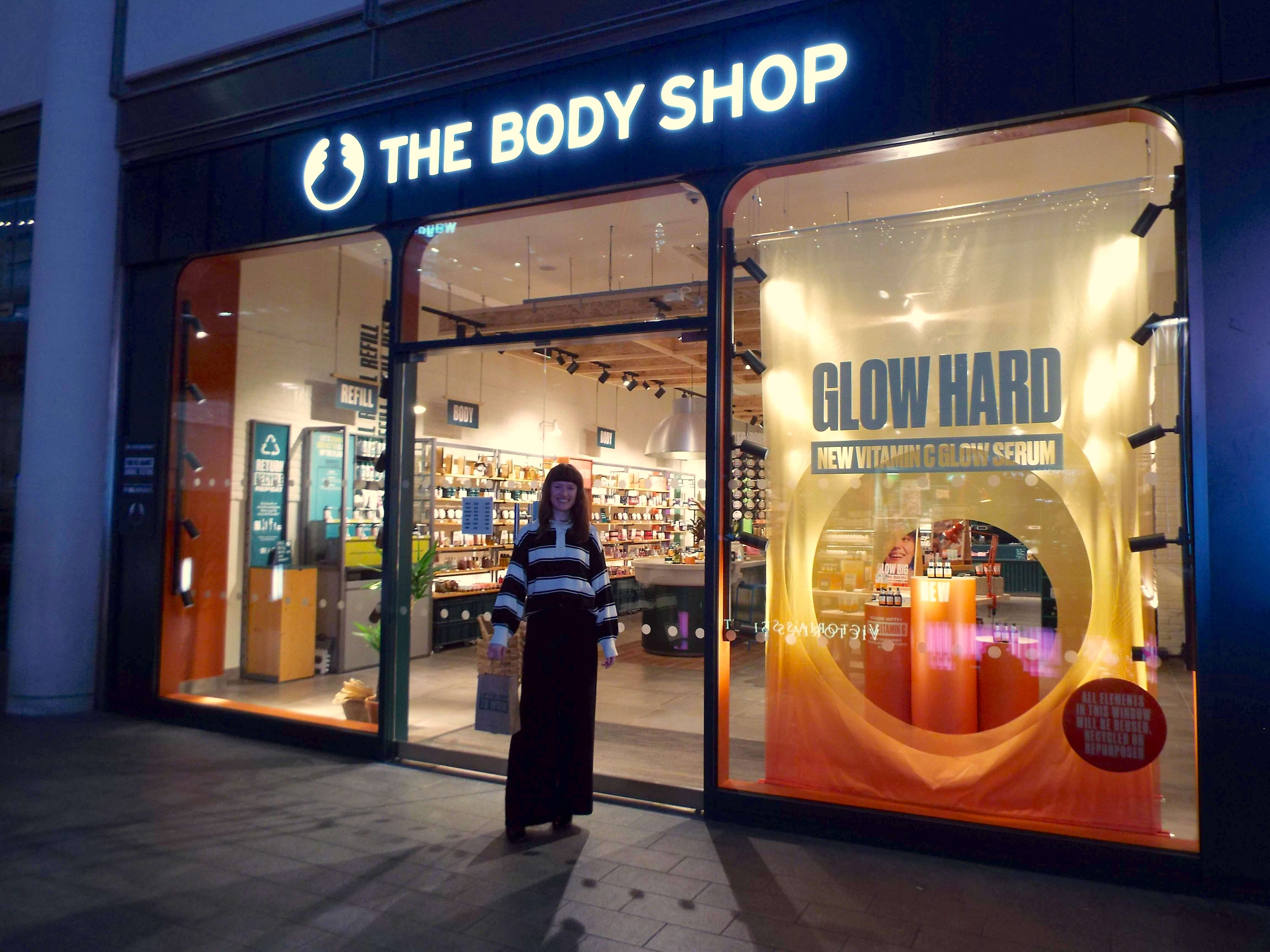 Again, Ellie posing outside the warmly-lit Body Shop store, with goodie bag.