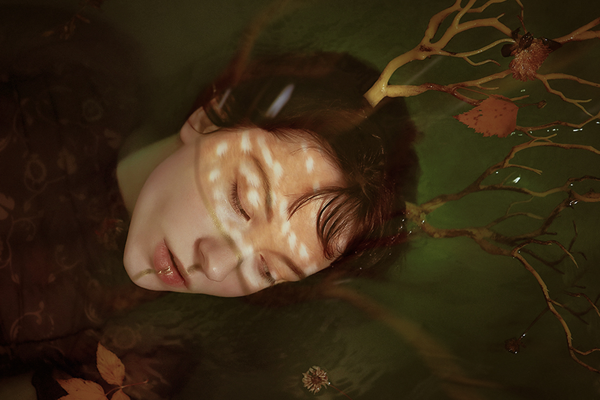 portrait of a beautiful young woman with dark fantasy makeup look, floating in a pool of green water