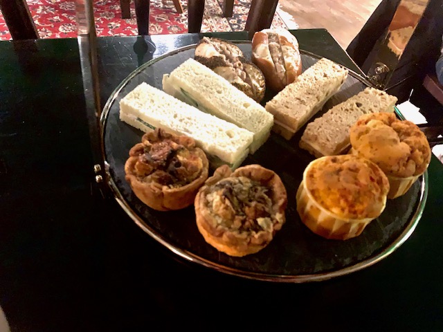 Cake stand of savouries including mini quiche, muffin and finger sandwiches