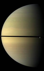 The moon Rhea, at far right, is dwarfed by Saturn. The shadow of another moon, Tethys, dots the disk at far left