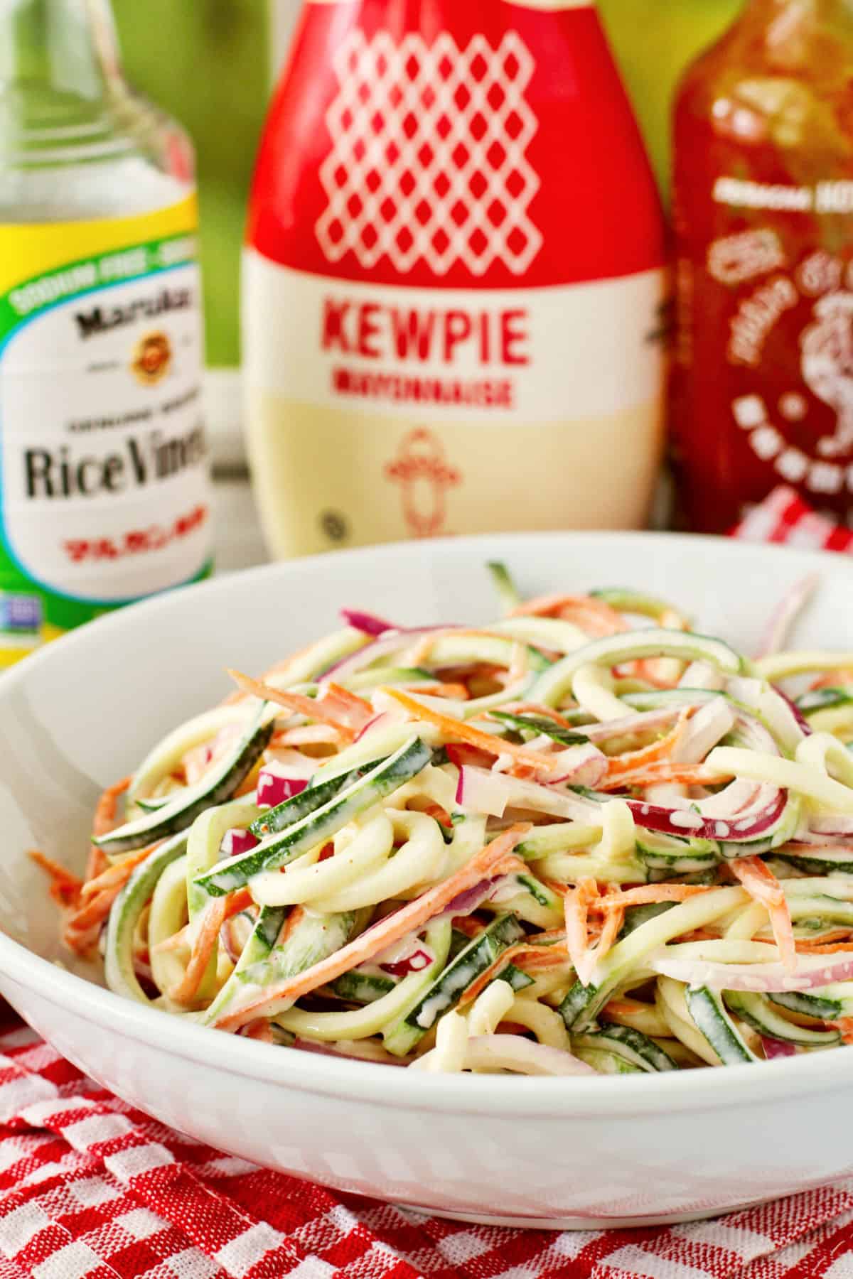 Zucchini Slaw in a serving bowl with the dressing ingredients in the background.