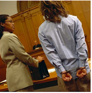 Photo of an African-American Criminal defense lawyer standing by a criminal with handcuffs on in court