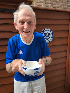 Photo Description- My dad a gentleman in his 80's standing in front of a wooden fence wearing a royal blue t-shirt and white shorts holding a blue and white cereal bowl carefully in both hands so that he doesn't drop it