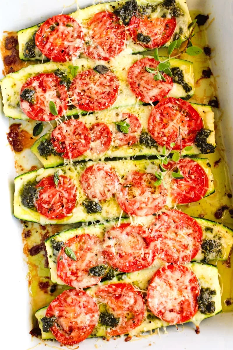 Top view closeup of Tomato and Pesto Stuffed Zucchini Boats in a white glass baking dish.