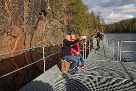 Kaksi henkeä ottamassa selfietä pystysuoran kallion edustalla kelluvalla kävelysillalla