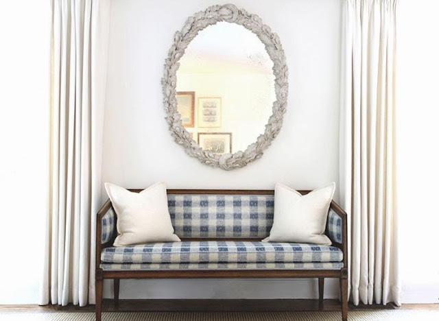 Blue and white gingham bench with white accent pillows and a round mirror with a baroque silver frame