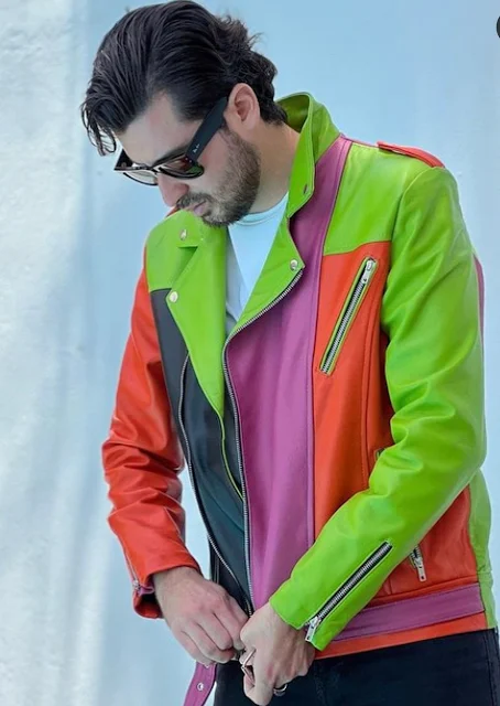 Man wearing oversized sunglasses zipping up a leather biker jacket that is neon green pink and orange sectioned pretty sexy jacket