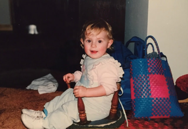 Toddler sitting in up-ended footstool, holding the legs.