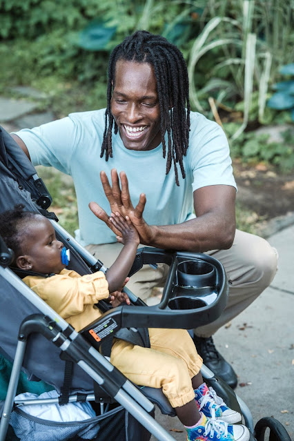 Man in dreadlocks high-fiving with his baby sitting on a stroller