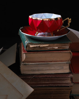 red tea cup and saucer on top of four old books