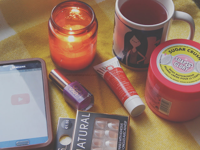 Flat lay picture with a phone, fake nails, nail polish, a face mask, candle, body butter, and a cup of tea.