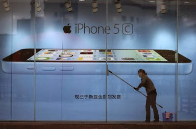 A worker cleans glass in front of an iPhone 5C advertisement at an apple store in Kunming, Yunnan province, in this October 27, 2013 file picture. CREDIT: REUTERS/WONG CAMPION