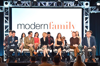 The whole cast of TV Sitcom Comedy "Modern Family" being interviewed under a backdrop of the show's logo.