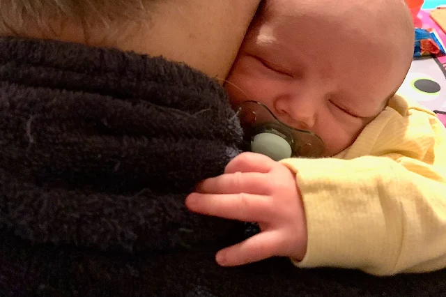 A newborn baby cuddled up to his parent who is thinking about all that is ahead in the first year of being a parent