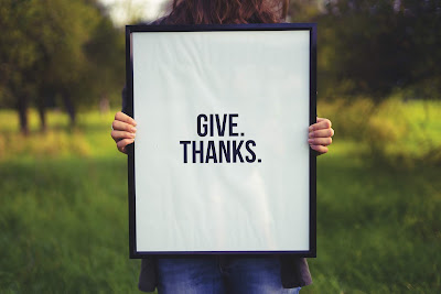 Mujer sosteniendo un cartel con la frase: give thanks