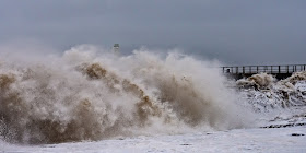 Photo of a huge wave almost obscuring the lighthouse on the end of the pier at Maryport