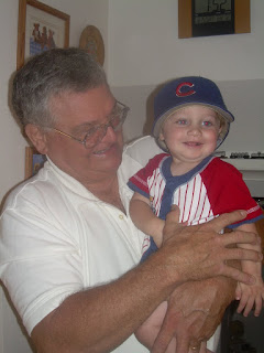 Photo of my dad holding my then one year old son who is wearing Grandpa's Cubs hat