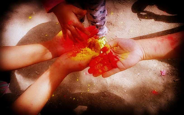 festival of colors, Holi. Red and yellow color in adult hands and a kid is picking up the color