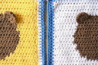 A close-up, top view of two squares side by side, yellow on the left and white on the right.  Only the vertical halves of each square can be seen showing one ear of each teddy face. The borders are alongside to show how the yellow square on the left has a border of one white row followed by a blue row while the white square on the right has a border of two blue rows.