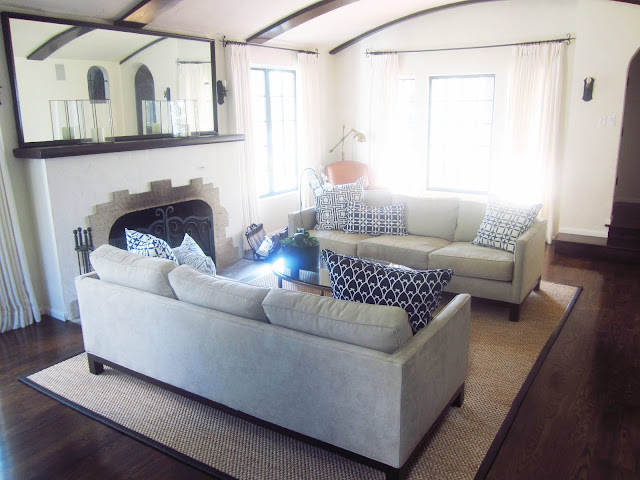 living room with dueling sofas with navy COCOCOZY linen pillows mixed and matched, an oval coffee table, floor length curtains and fireplace with a large mirror on it's mantel