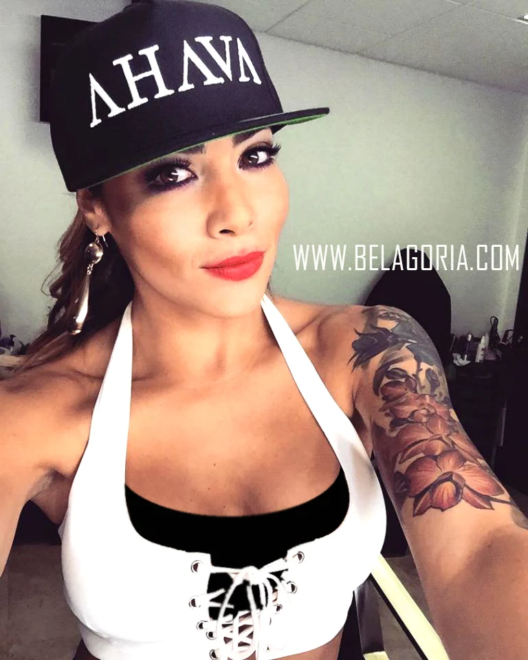 modelo latina con gorra, sujeta la camara mientras se fotografia lleva tatuajes por todos los brazos