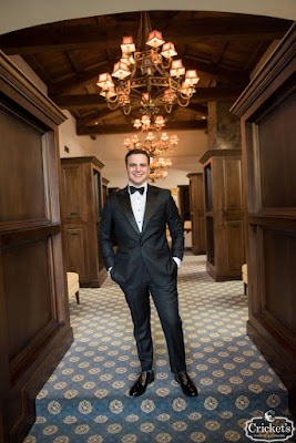 groom posing with hands in black suit pockets in mens locker room