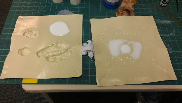 On a green cutting board sits two pages of tan Braillon.  Each page is acting like a mold.  The page on the left has two of Mars' moons (lopsided and oval in shape), a canyon (oval and bumpy with a smooth crevice in the middle), and a 2.5 inch in diameter circle filled with the white casting resin that will become the new mold of the character of Mars.  The page on the right features Little Star being born and the white resin is pooled in a smaller circle of about 1.5 inches in diameter and in curved lines spreading away from the circle - 3 on each side).