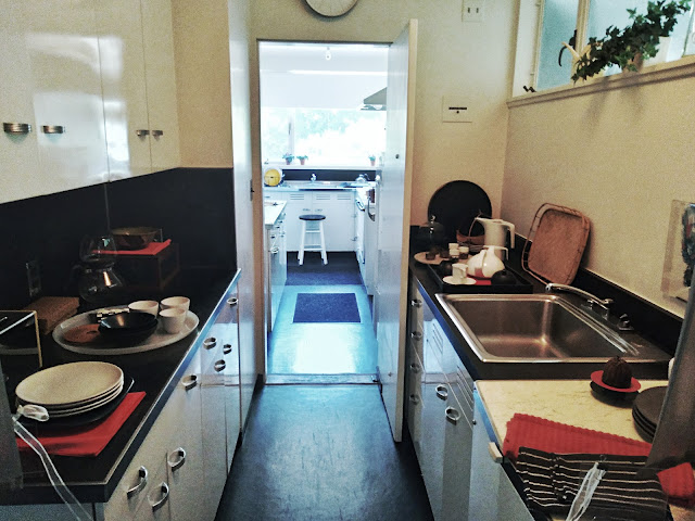 A regular kitchen in the background, with a door leading to an industrial style kitchen with metal cabinets in the foreground.
