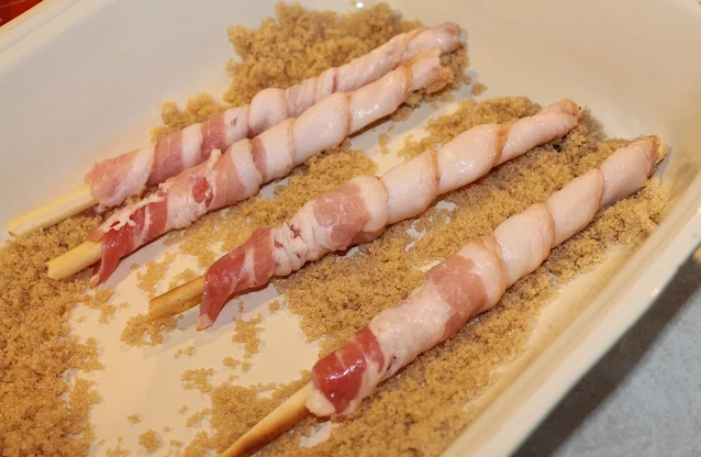 Bacon wrapped breadsticks in a dish with brown sugar.