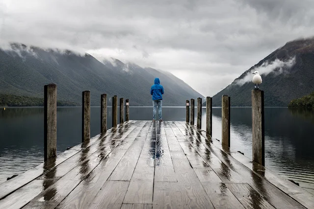 Person lost in thoughts during rain, sitting alone in nature, feeling peace and solitude.