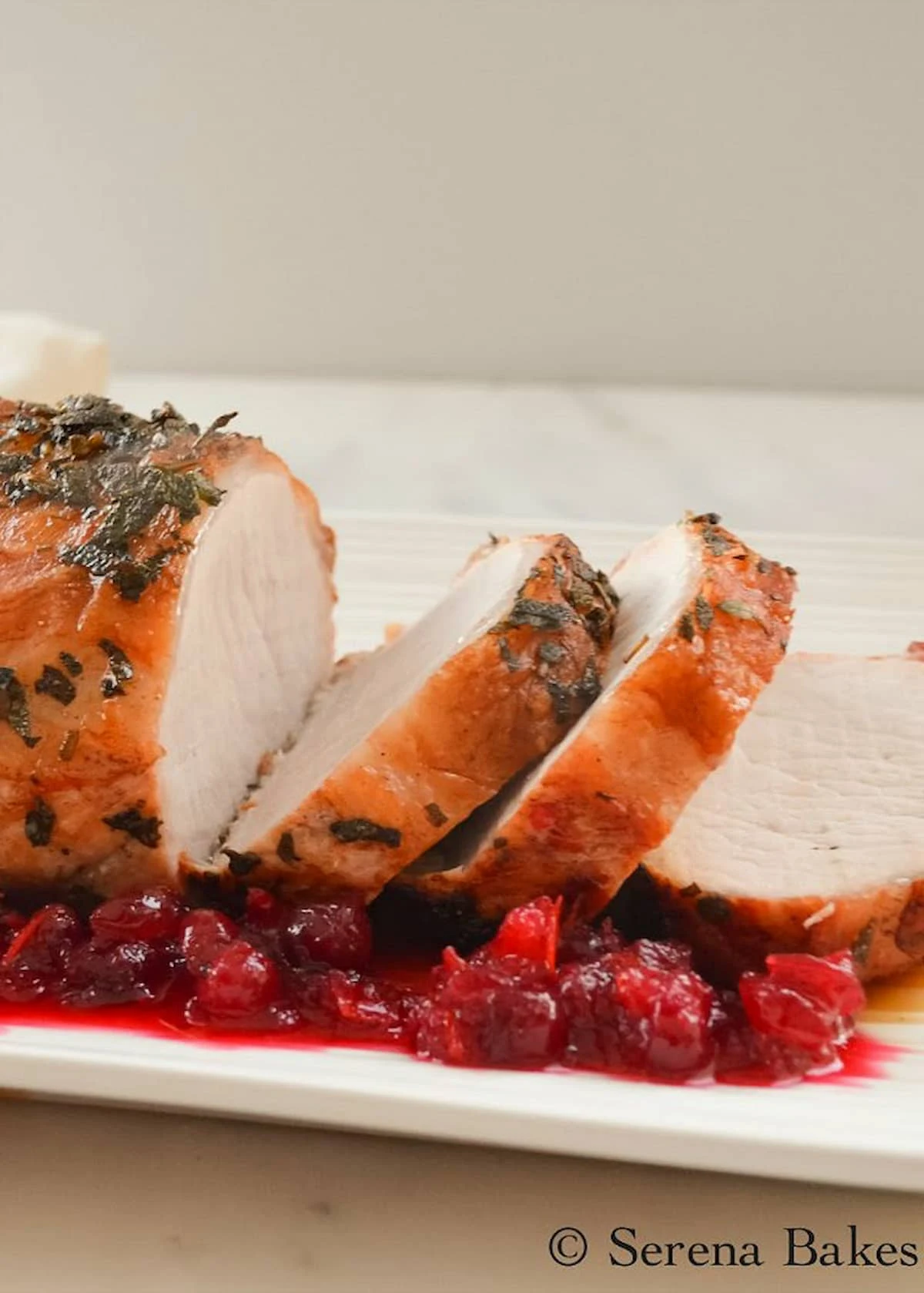 A side shot of a sliced Rosemary Sage Pork Loin Roast on a white tray with Orange Cranberry Sauce along the edge.