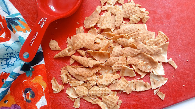 crumbled sugar cone pieces for the Loaded Coffee Ice Cream sitting on a red cutting board next to a measuring cup and a floral towel