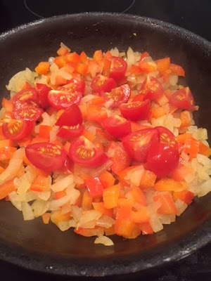 Softened red pepper and onion in a frying pan with cherry tomatoes on top