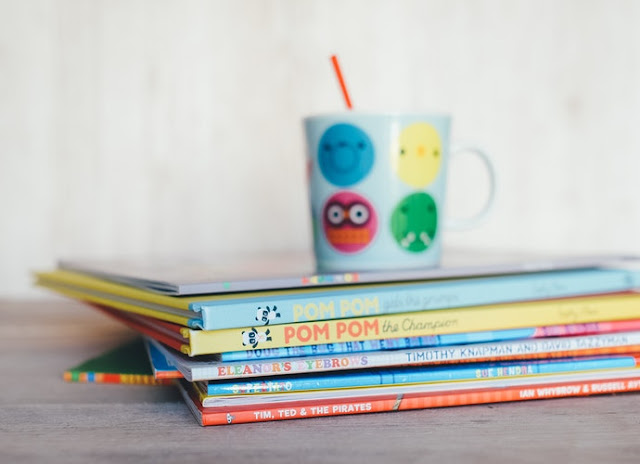 Pile of children's books with a kids cup and straw on top of them