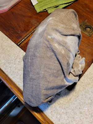 A linen napkin has water drops on it and is wrapped around the Lekue.