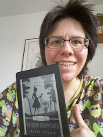 das Bild zeigt die Buchbloggerin mit dem Kindle in der Hand. Das Cover zeigt die Silhouette von Jill und ihrem Kater