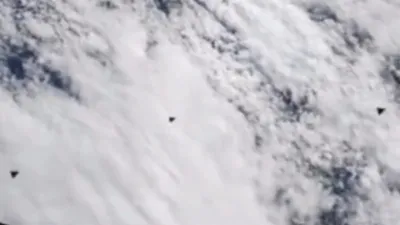 There's 3 black triangle shaped UFOs flying straight past the ISS.
