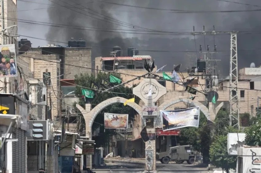 Fumaça sobe atrás de edifícios e acima de um veículo blindado militar israelense durante uma operação na cidade de Jenin, na Cisjordânia | Jaafar Ashtiyeh/AFP