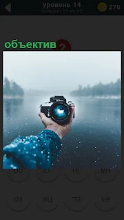 на фоне озера протянута рука для селфи, в которой обьектив фотоаппарата
