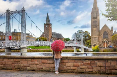 Uma turista com um guarda-chuva de padrão escocês desfruta da vista para a paisagem urbana de Inverness, Escócia, durante o outono