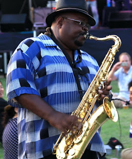 Image of man with striped blue shirt playing a saxophone