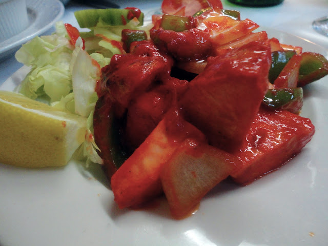 verduras y pollo con salsa roja junto a ensalada