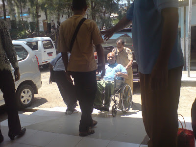 Beberapa orang sedang mendorong seorang bapak dengan kursi roda didepan poliklinik penyakit dalam.
