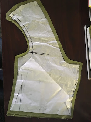 A tissue-paper vest front pattern with a sharply angled strap, pinned to a piece of green linen cut slightly larger.