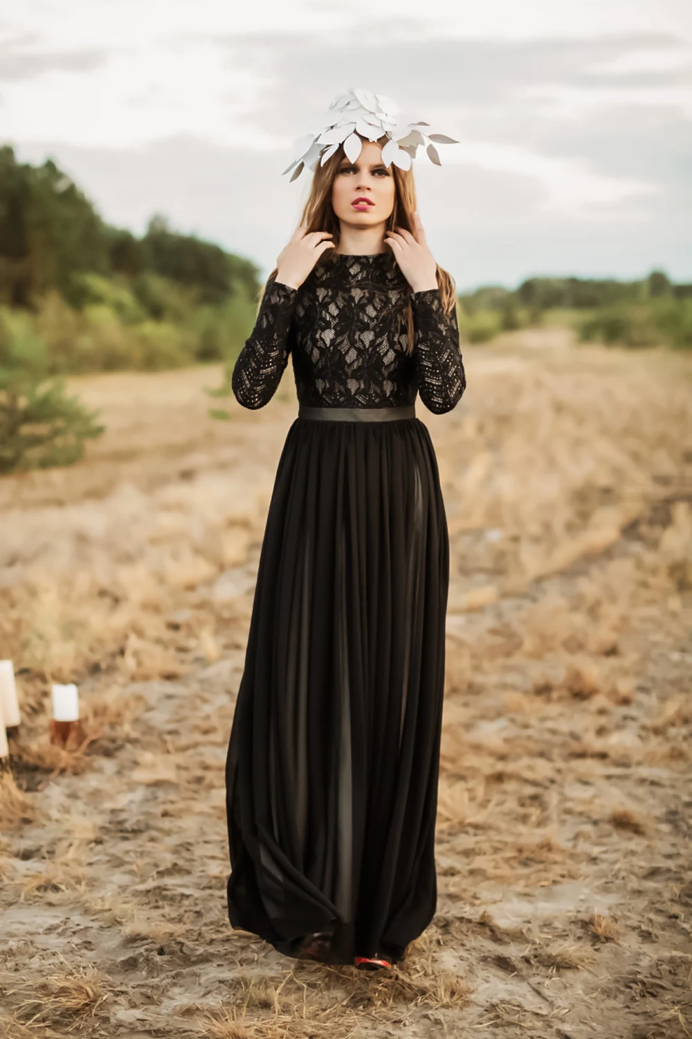 woman in black bridal dress with flower crown on her head is posing in a field.