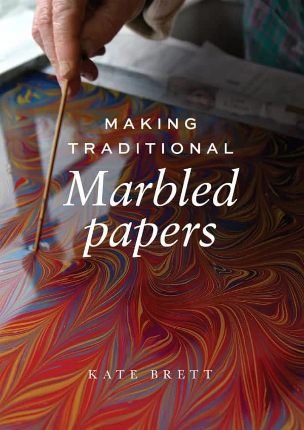book cover depicting hand holding wooden dowel swirling floating paint to create marbled design