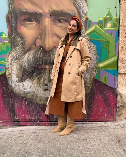 woman in a trench coat in Jerusalem against a graffiti wall